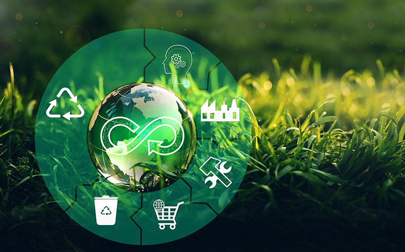 A glass globe with a circular economy symbol sits on grass, surrounded by eco icons including recycling, innovation, industry, repair, waste, and shopping, symbolizing sustainable and green business practices.