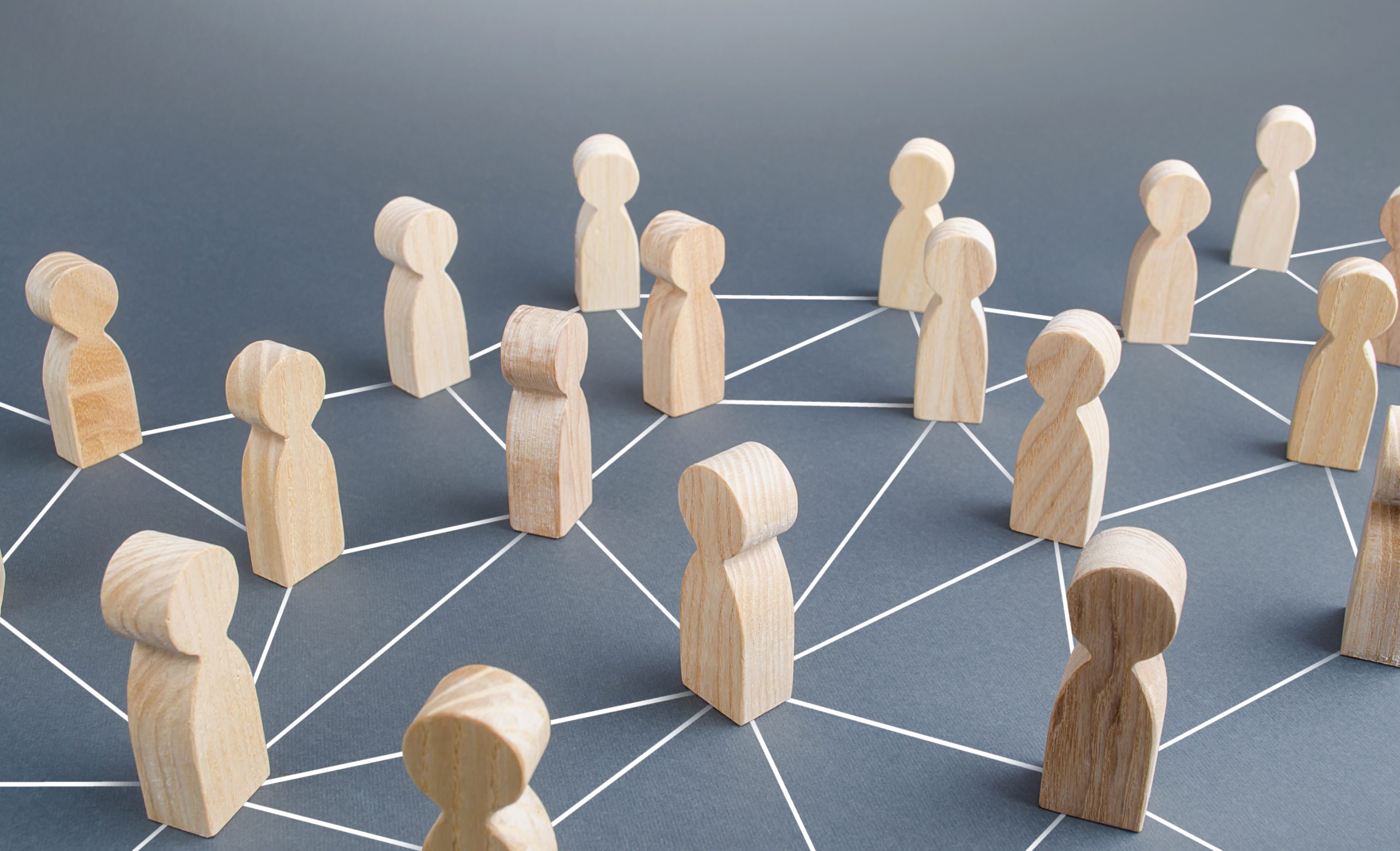 Wooden figurines stand on a dark surface, connected by white lines forming a network, symbolizing social or professional connections and communication within a community.